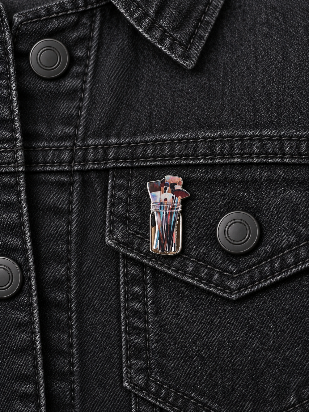 Artist Paintbrushes Jar Pin displayed on a black denim jacket beside a metal button