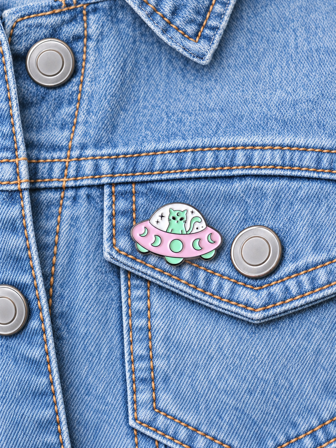 Alien Cat UFO Pin displayed on a light-wash denim jacket beside a metal button