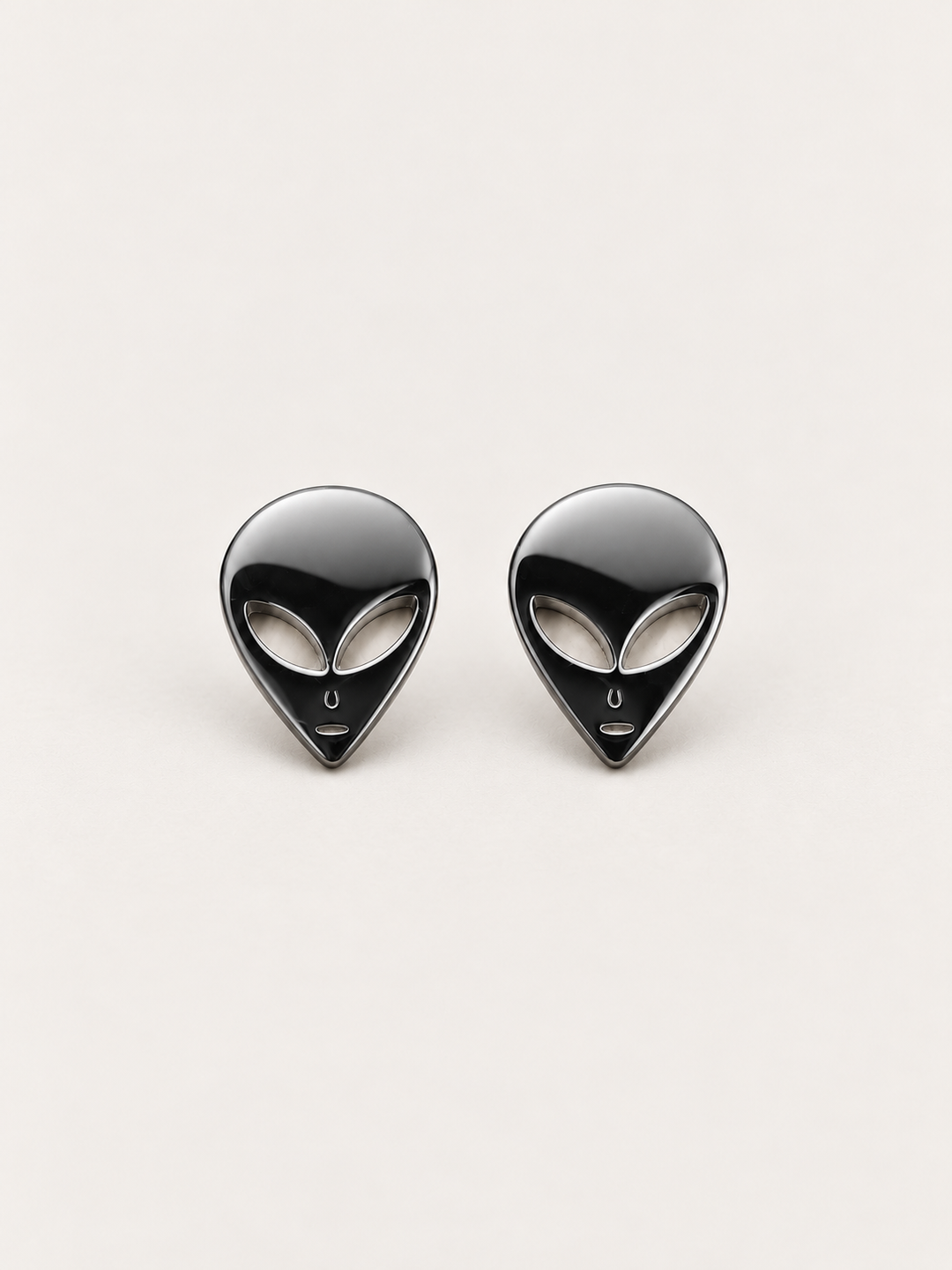 Black Alien Head Stud Earrings shown angled on a warm neutral background