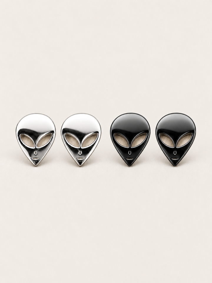 Alien Head Stud Earrings in silver and black stainless steel on a warm neutral background