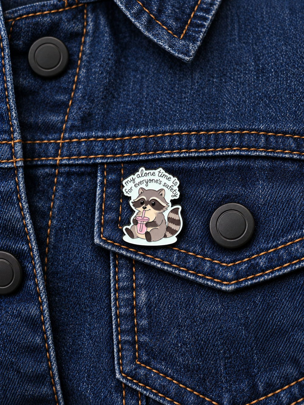 Alone Time Raccoon Pin displayed on dark indigo denim beside a matte black button