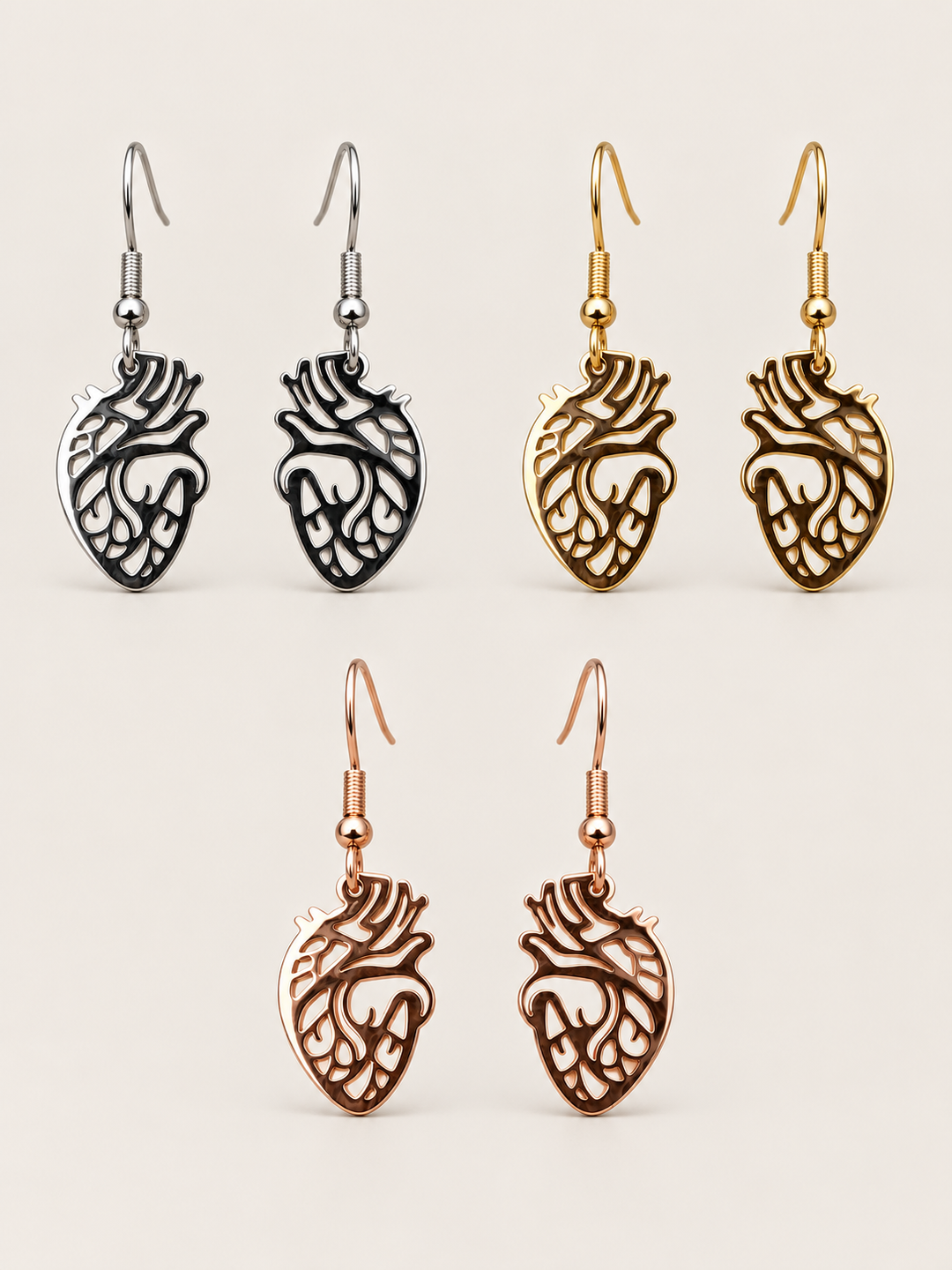 Anatomical Heart Drop Earrings in silver, gold, and rose gold on a warm neutral background