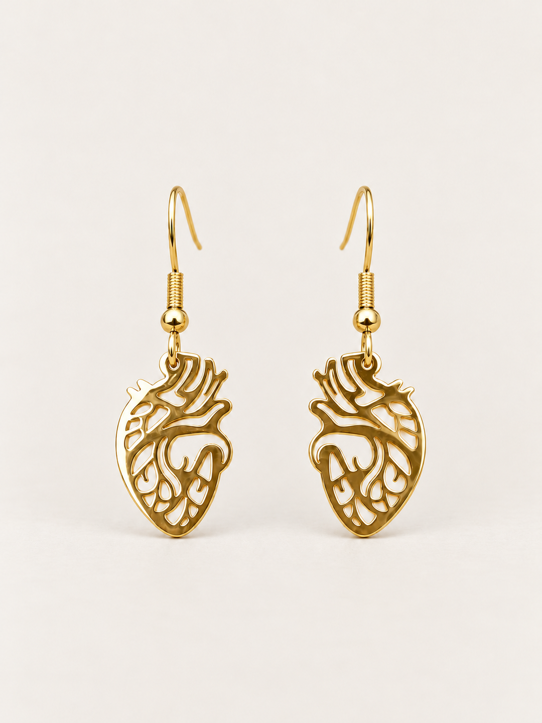 Anatomical Heart Drop Earrings in gold shown on a warm neutral background