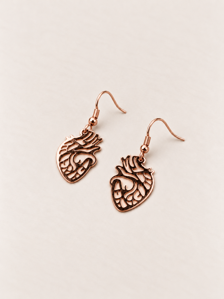 Anatomical Heart Drop Earrings in rose gold lying flat on a warm neutral surface