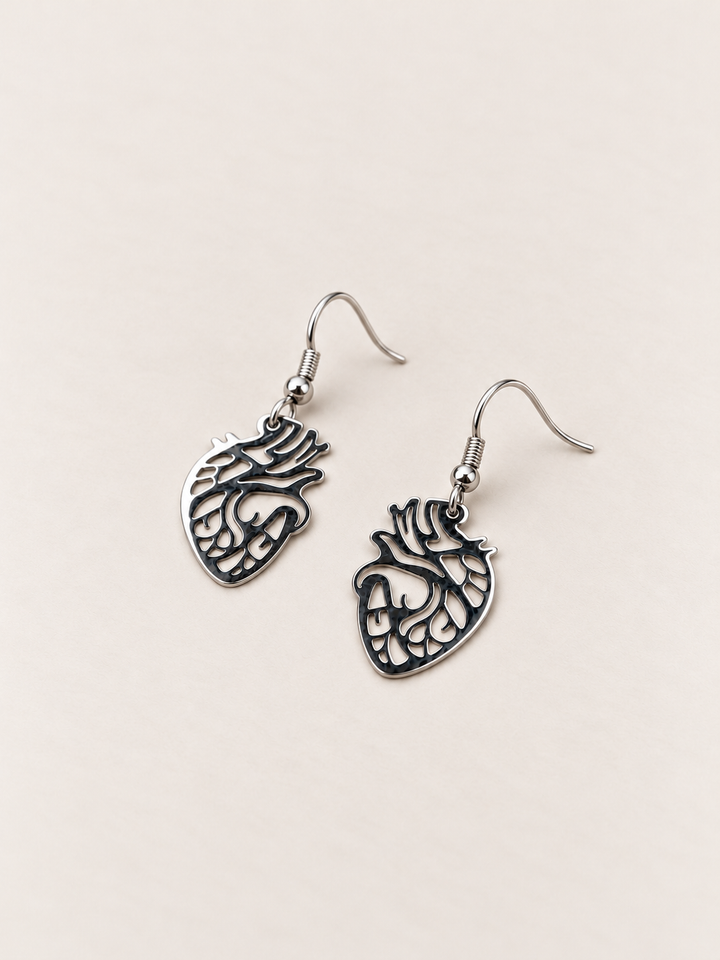 Anatomical Heart Drop Earrings in silver lying flat on a warm neutral surface