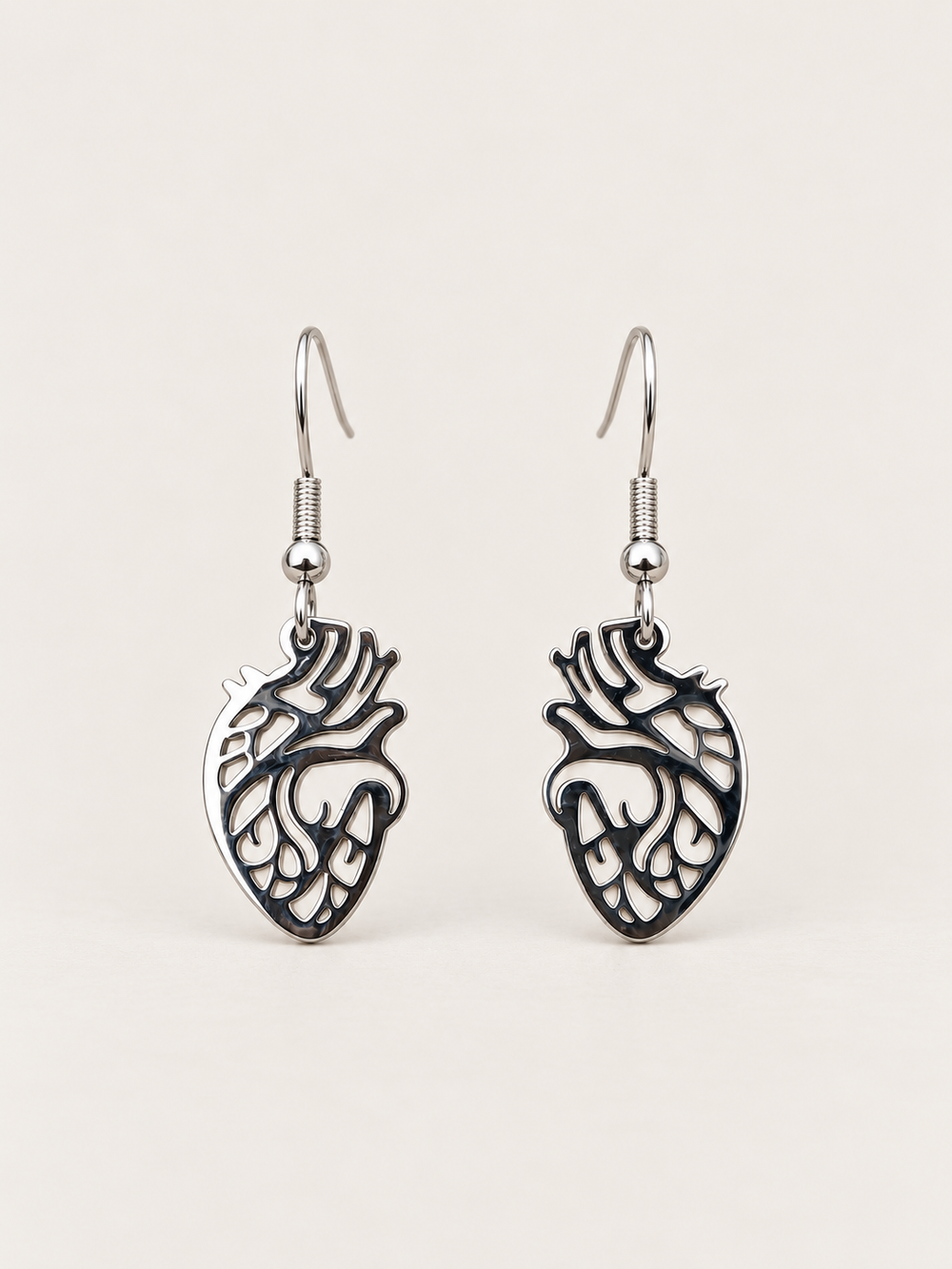 Anatomical Heart Drop Earrings in silver shown on a warm neutral background