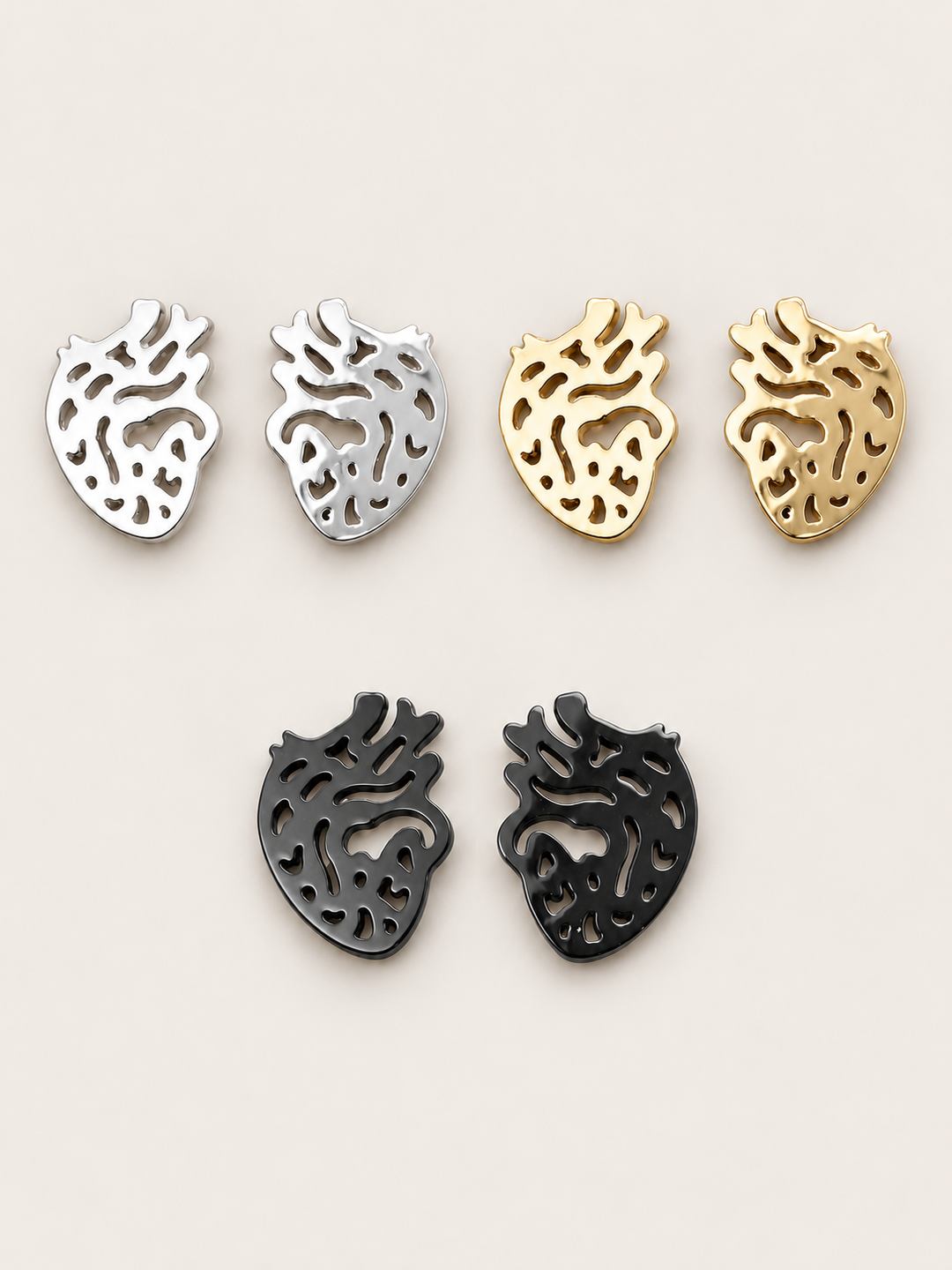 Anatomical Heart Stud Earrings in Silver, Gold, and Black on a warm neutral background