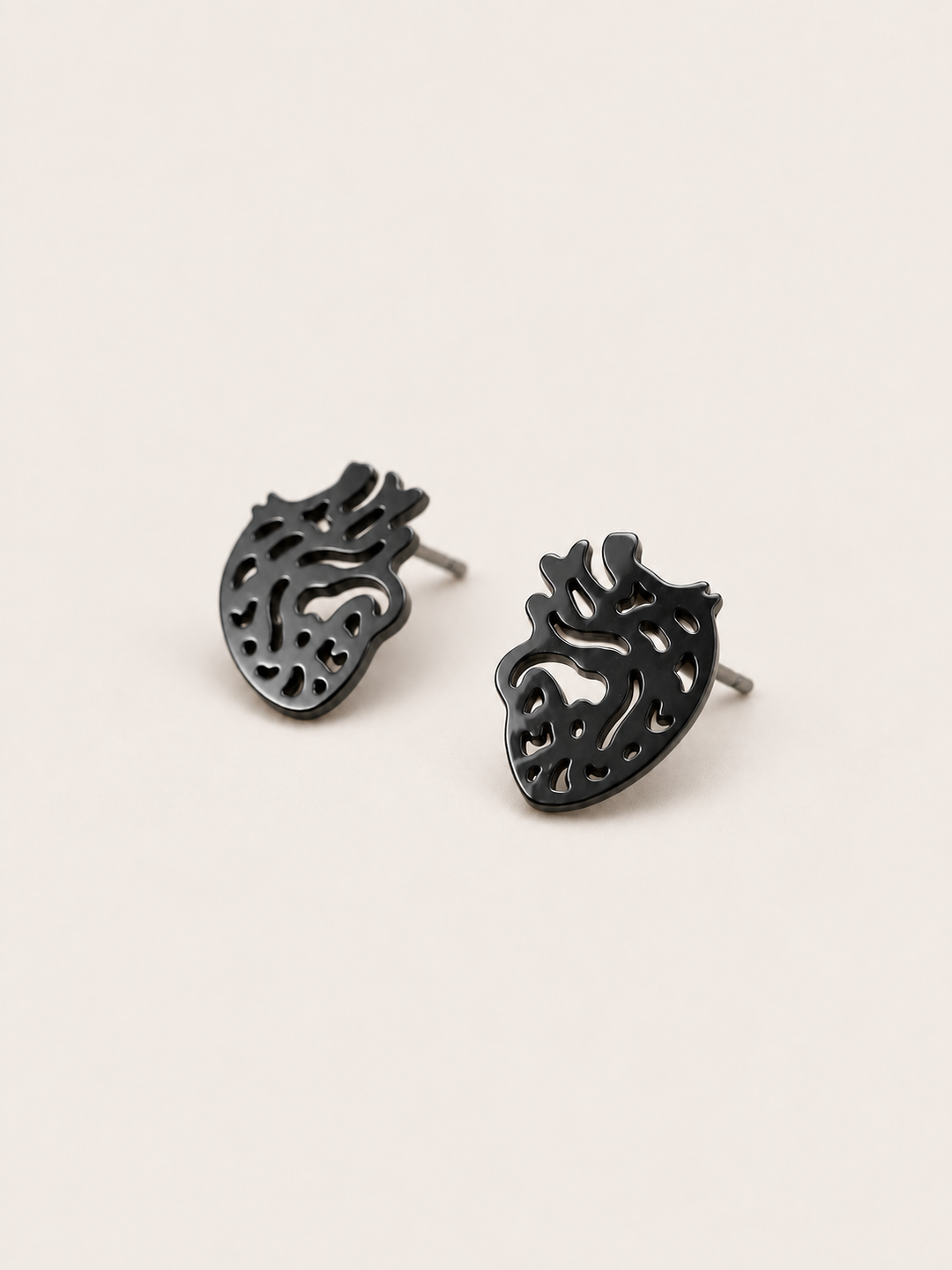 Anatomical Heart Stud Earrings in black shown angled on a warm neutral background