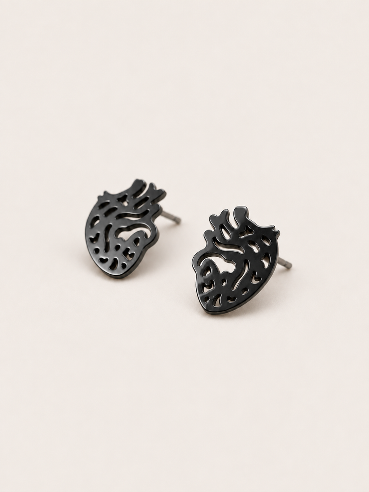 Anatomical Heart Stud Earrings in black shown angled on a warm neutral background