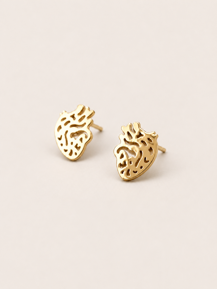 Anatomical Heart Stud Earrings in gold shown angled on a warm neutral background