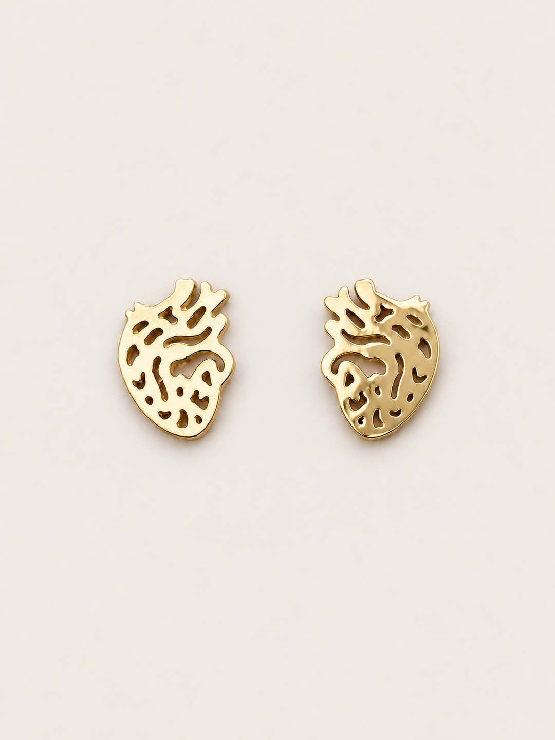 Anatomical Heart Stud Earrings in gold shown on a warm neutral background