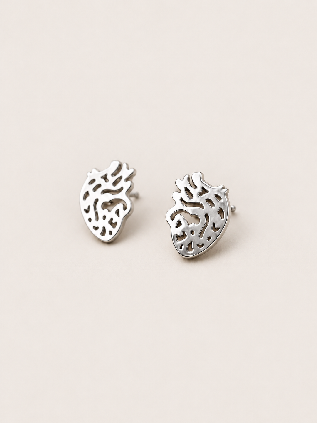 Anatomical Heart Stud Earrings in silver shown angled on a warm neutral background
