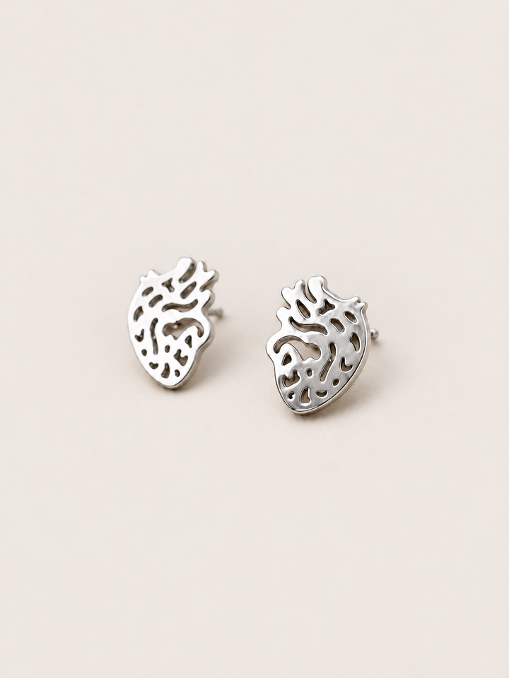 Anatomical Heart Stud Earrings in silver shown angled on a warm neutral background