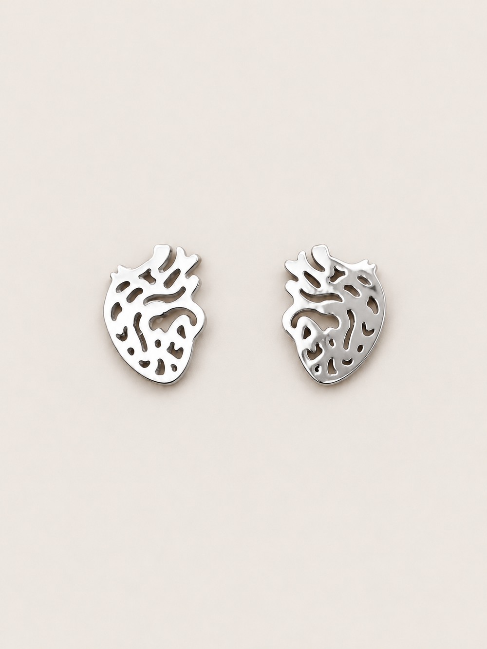 Anatomical Heart Stud Earrings in silver shown on a warm neutral background