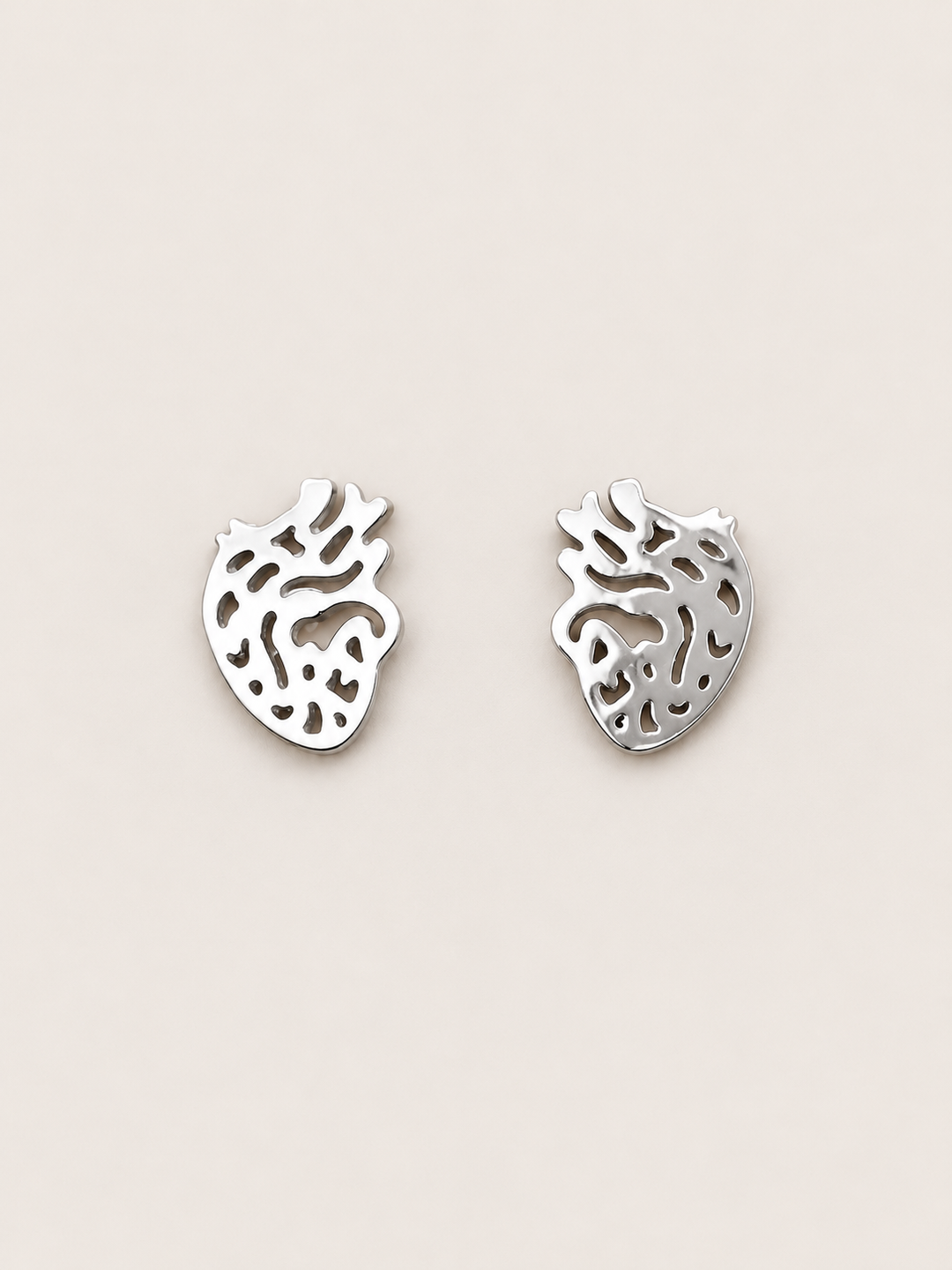 Anatomical Heart Stud Earrings in silver shown on a warm neutral background