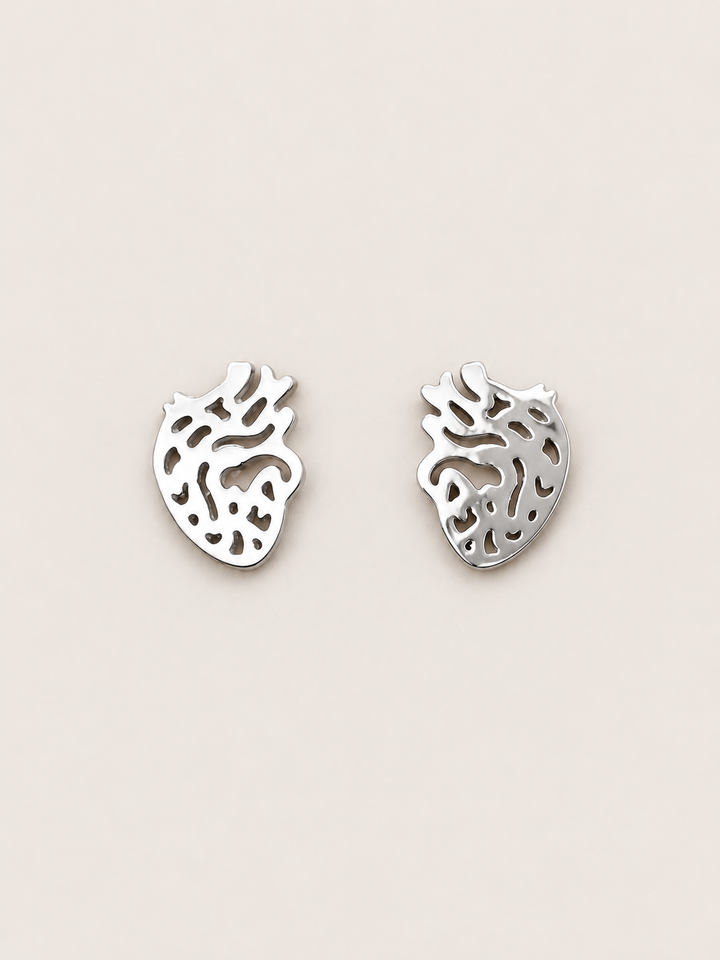 Anatomical Heart Stud Earrings in silver shown on a warm neutral background