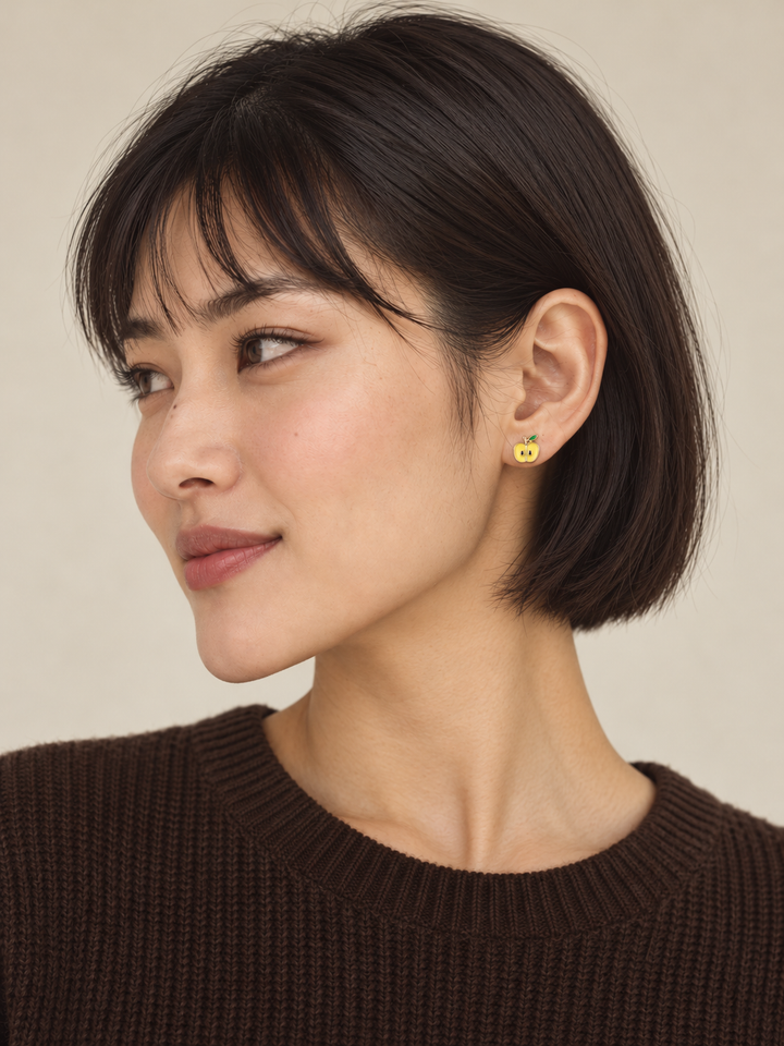 Yellow apple-half stud worn on the viewer-right ear