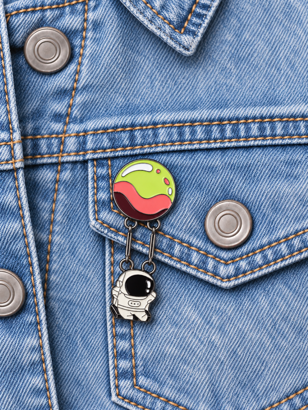 Astronaut Hanging from Planet Pin displayed on a light-wash denim jacket beside a metal button