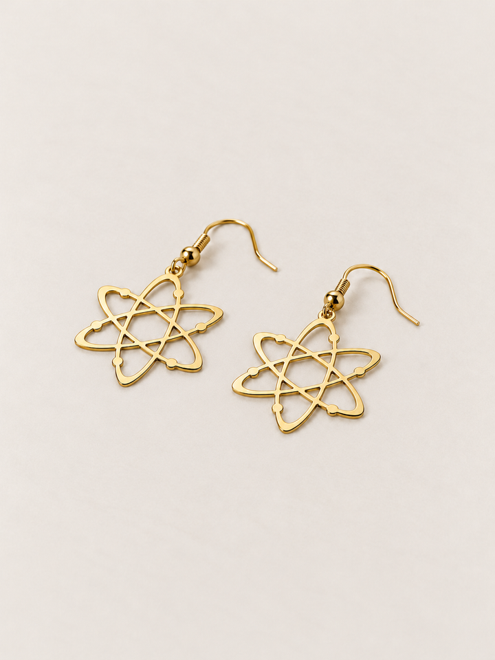 Gold Atom Drop Earrings lying flat at an angle on a warm neutral background