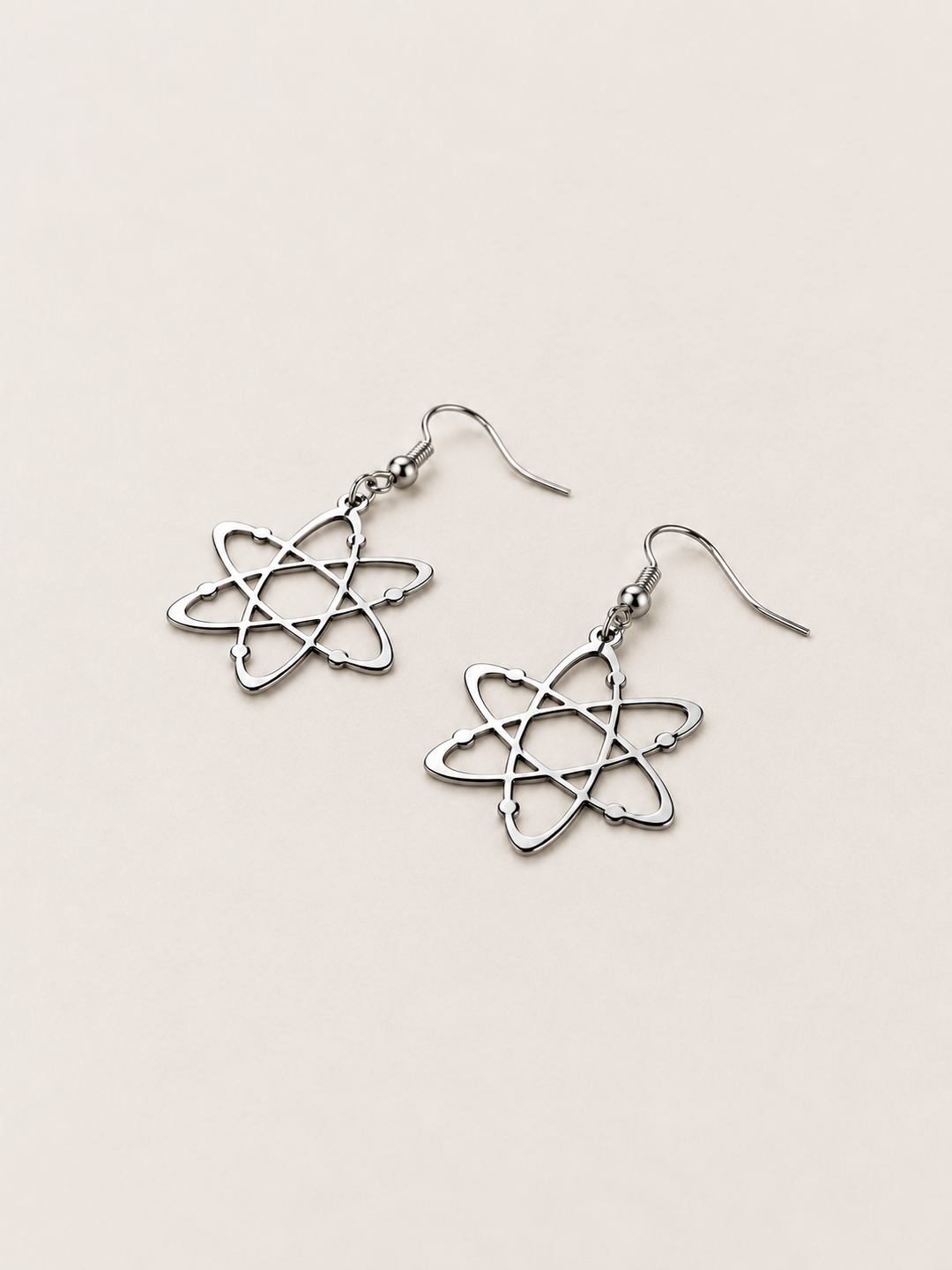 Silver Atom Drop Earrings lying flat at an angle on a warm neutral background