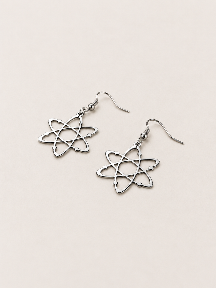 Silver Atom Drop Earrings lying flat at an angle on a warm neutral background