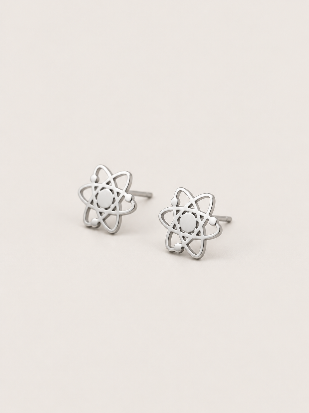Atom Stud Earrings in silver shown at an angle on a warm neutral background