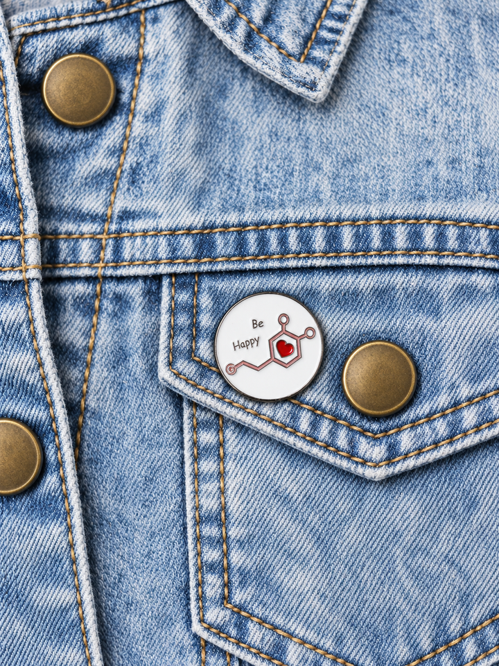 Be Happy Chemistry Pin displayed on pale acid-wash denim beside a brass button