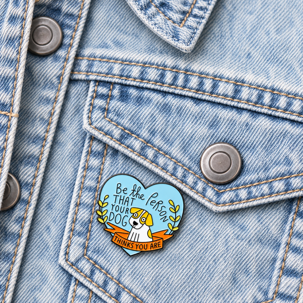 Be the Person Your Dog Thinks You Are Pin displayed on a blue denim jacket beside a metal button