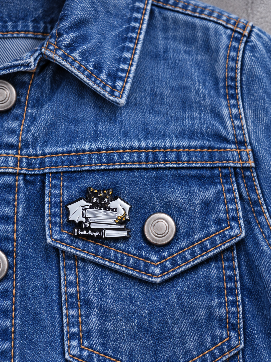 Black Book Dragon Pin displayed on acid-wash denim beside a metal button