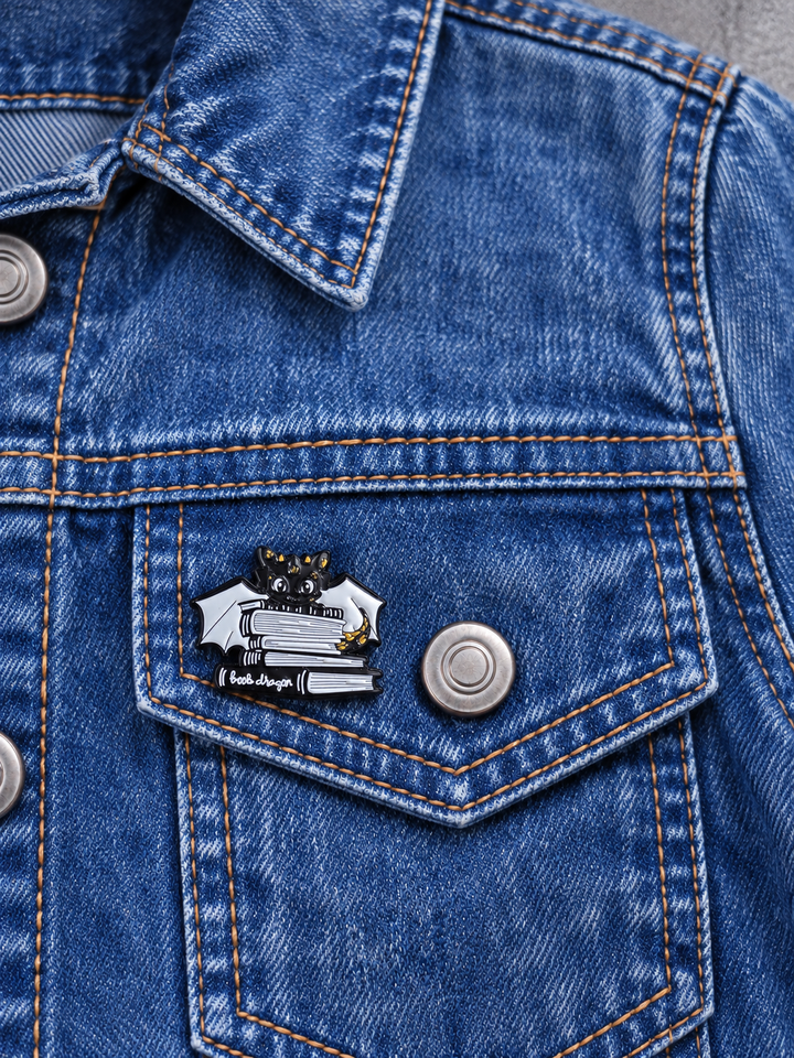 Black Book Dragon Pin displayed on acid-wash denim beside a metal button