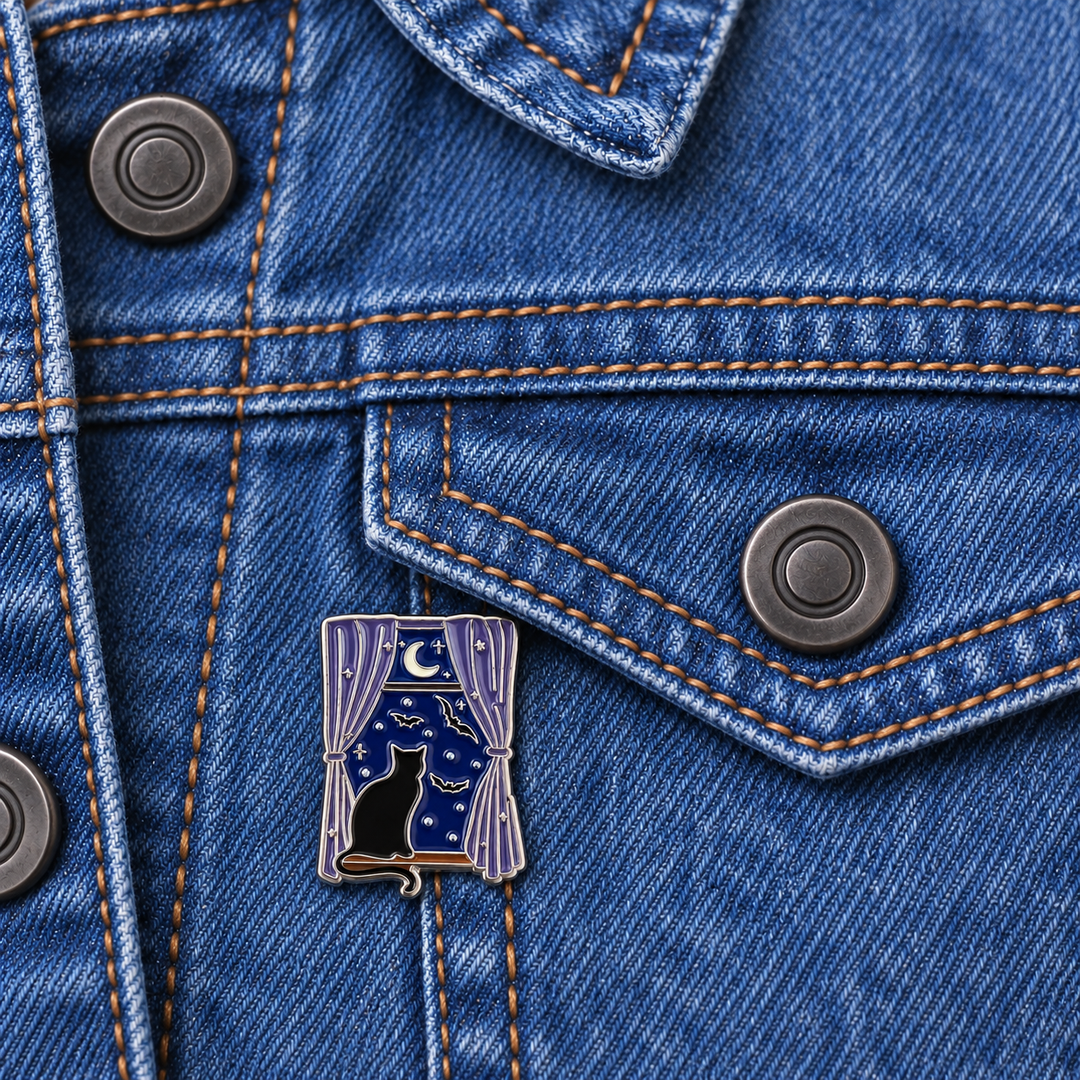 Black Cat Moonlit Window Pin displayed on a blue denim jacket beside a metal button