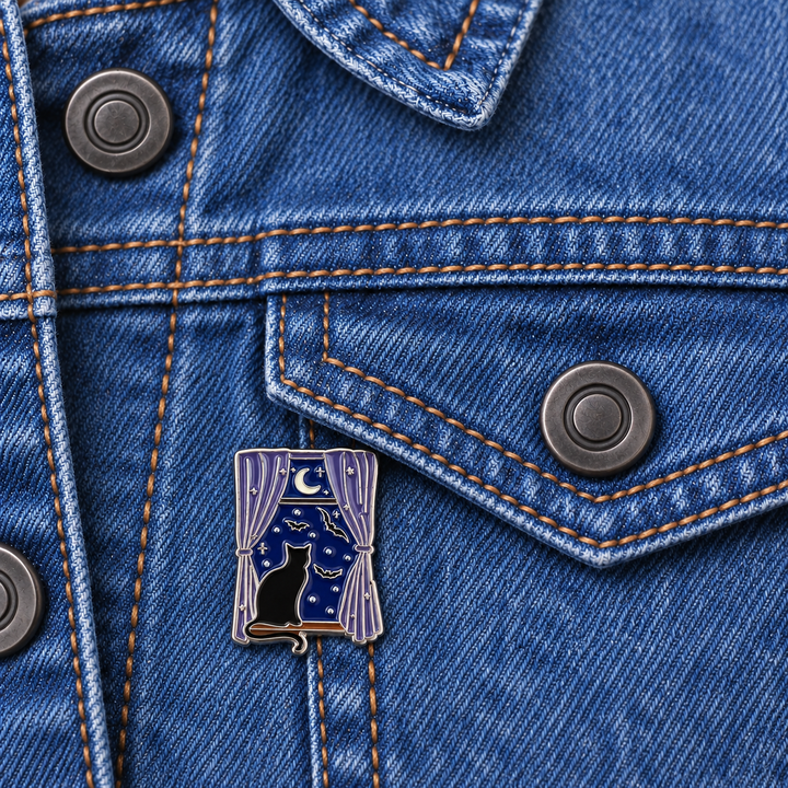 Black Cat Moonlit Window Pin displayed on a blue denim jacket beside a metal button