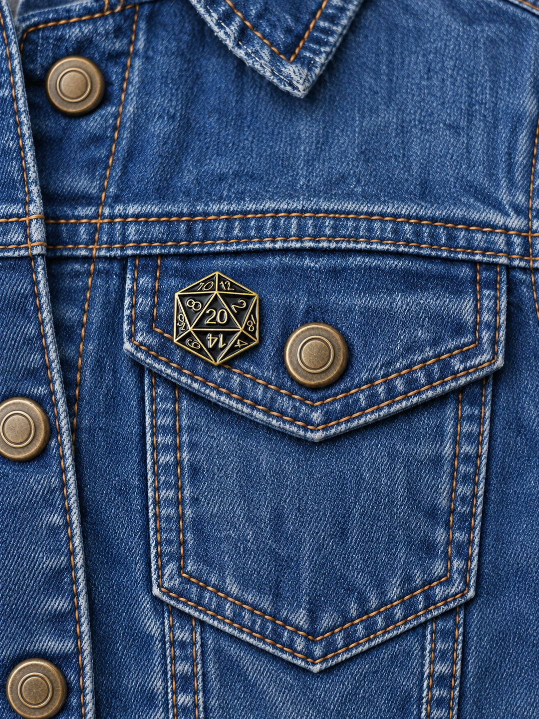 Black Gold D20 Dice Pin displayed on a vintage faded denim jacket beside a metal button