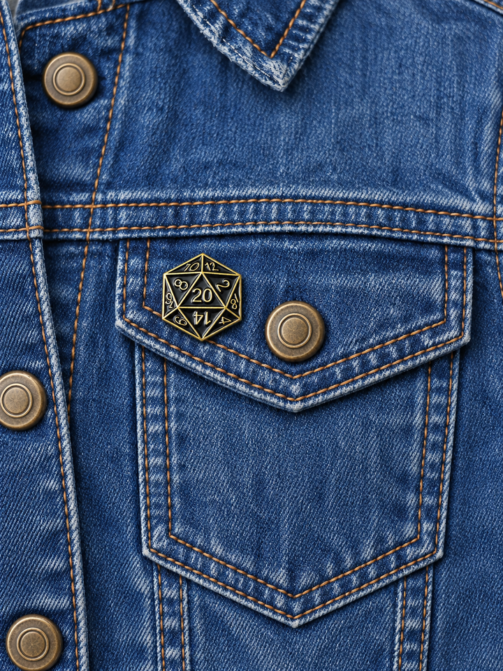 Black Gold D20 Dice Pin displayed on a vintage faded denim jacket beside a metal button