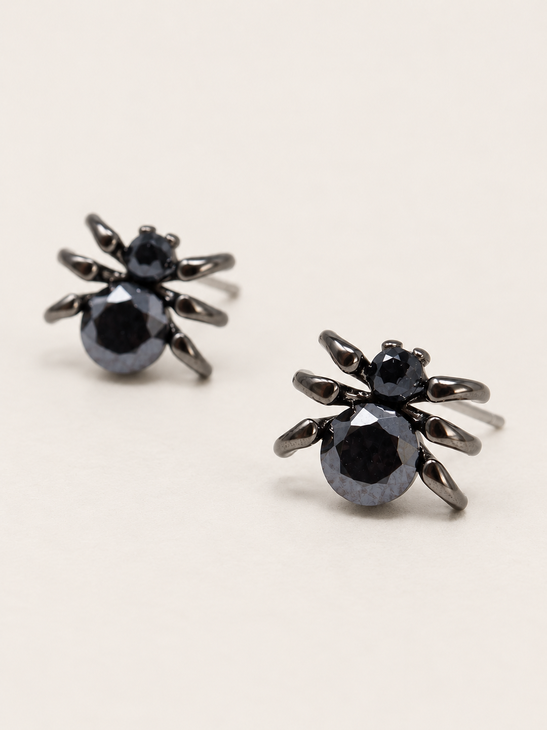 Black Spider Stud Earrings shown angled on a warm neutral background