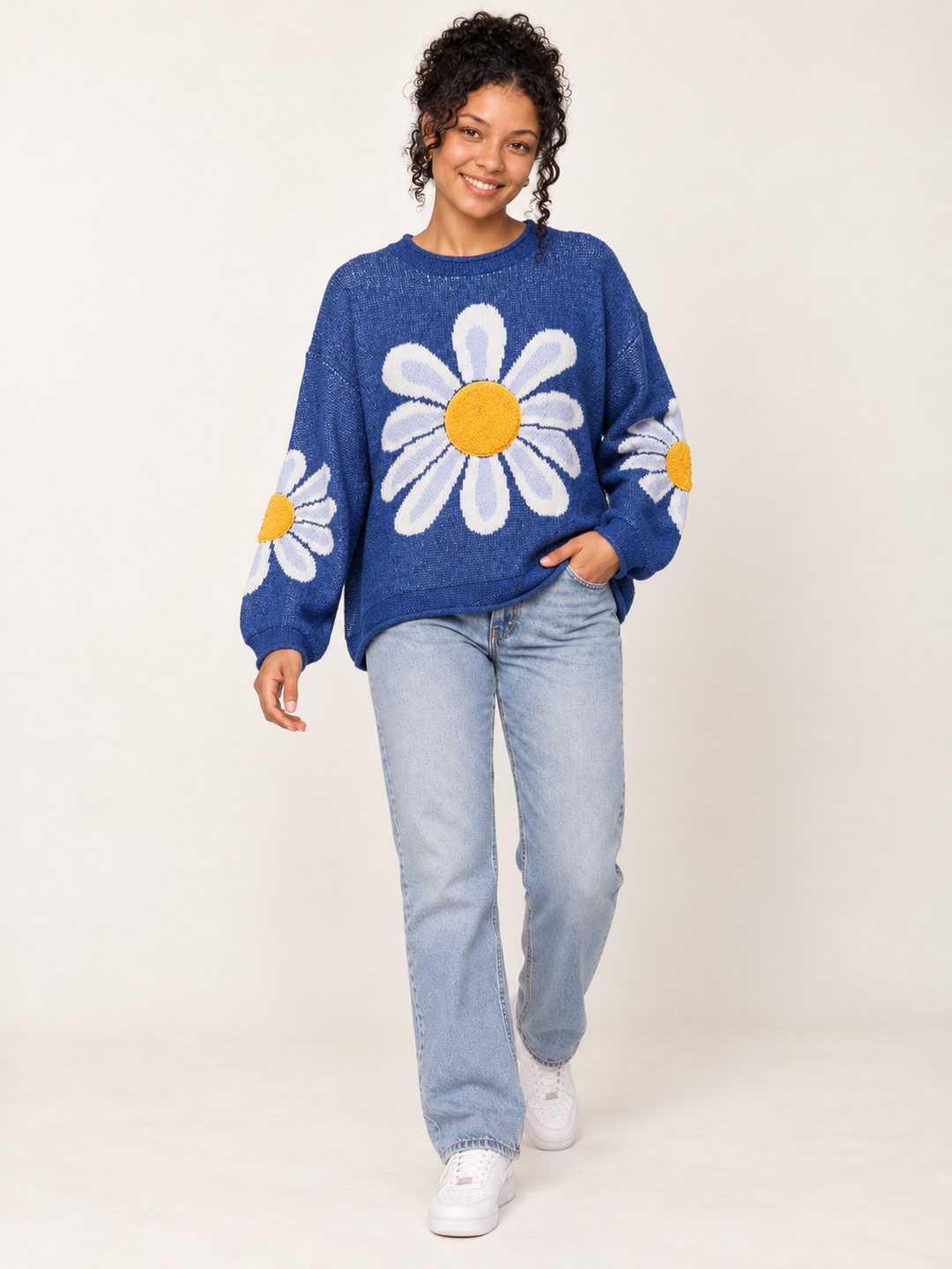 Full-body view of model wearing oversized blue daisy sweater with light-wash jeans