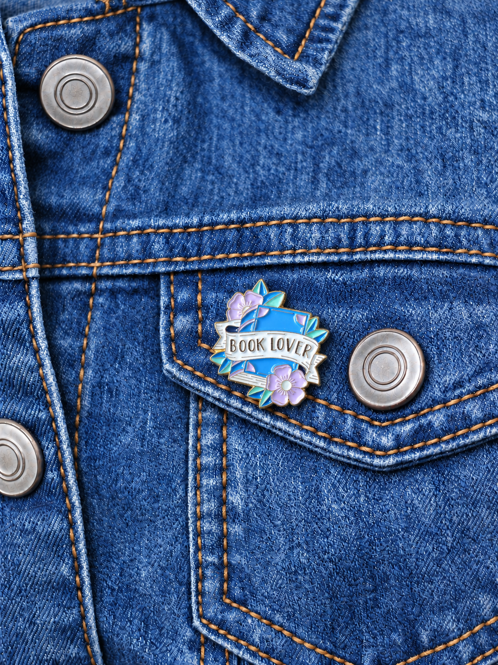 Book Lover Floral Pin displayed on a blue denim jacket beside a metal button