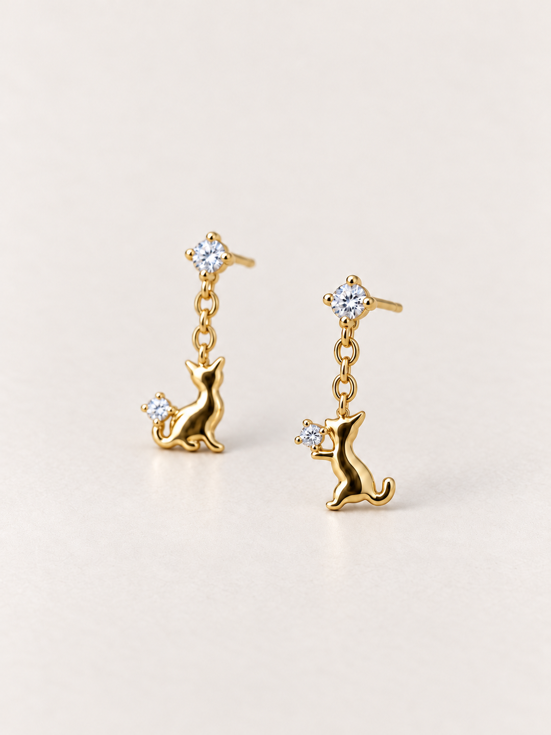 Gold Cat Crystal Drop Earrings shown angled on a warm neutral background