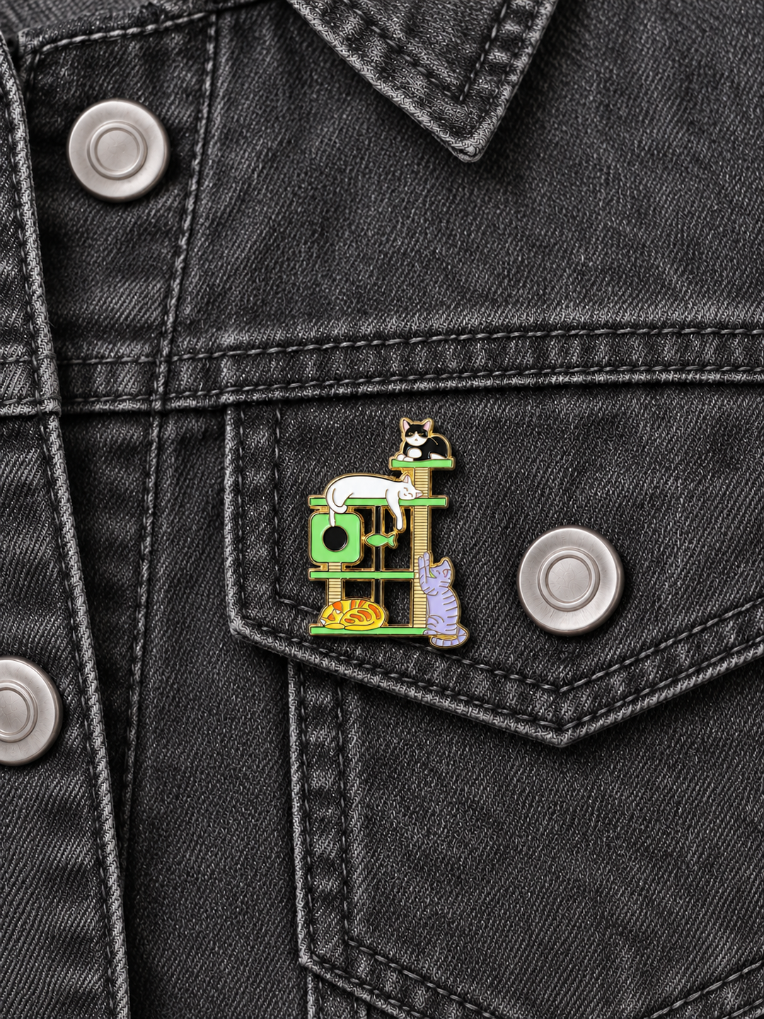 Cats on Cat Tree Pin displayed on a charcoal denim jacket beside a metal button