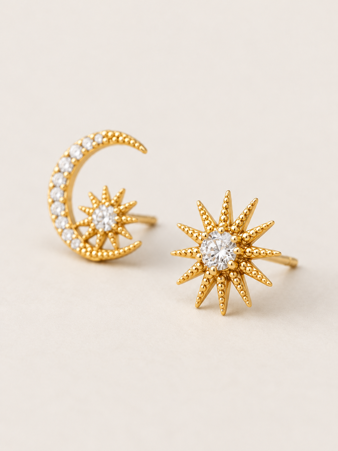 Gold Celestial Moon and Starburst Earrings shown angled on a warm neutral background