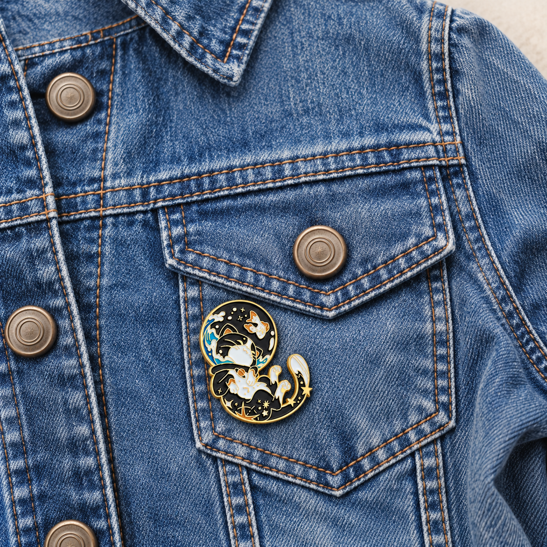 Cosmic Cats Space Pin displayed on a blue denim jacket beside a metal button