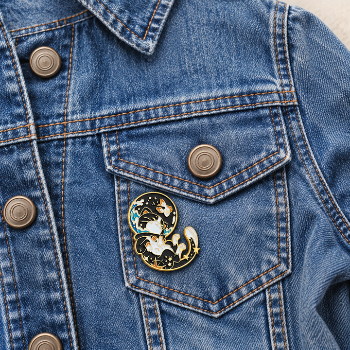 Cosmic Cats Space Pin displayed on a blue denim jacket beside a metal button