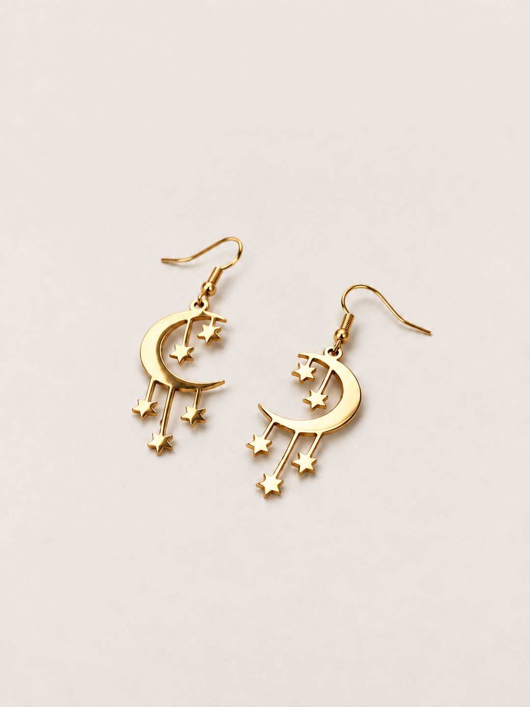 Gold Crescent Moon and Stars Drop Earrings lying at an angle on a warm neutral background