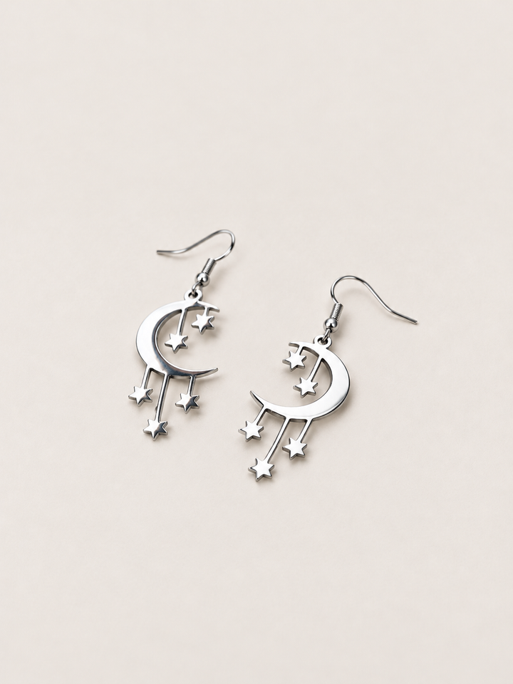 Silver Crescent Moon and Stars Drop Earrings lying at an angle on a warm neutral background
