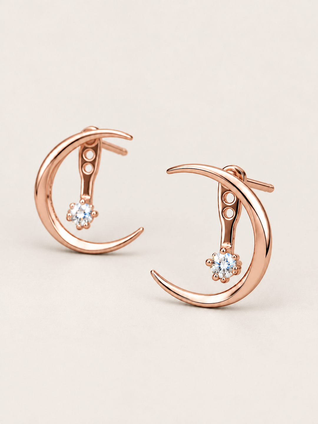 Crescent Moon Ear Jacket Earrings in Rose Gold shown angled on a warm neutral background