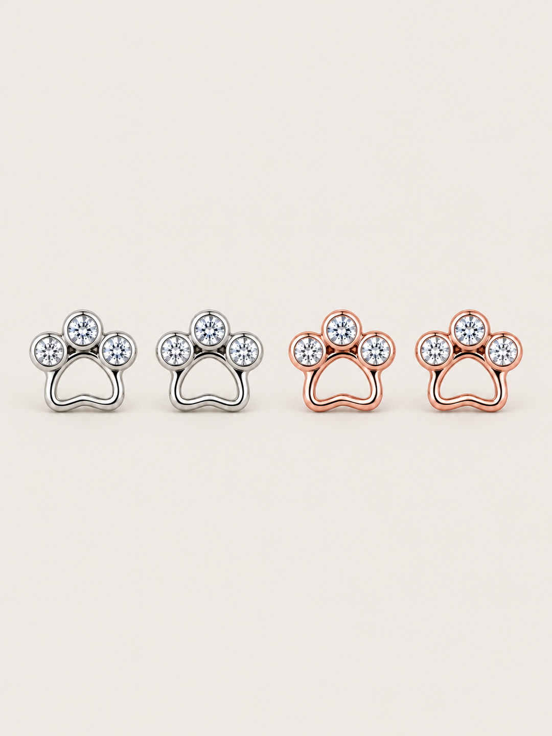 Crystal Paw Print Stud Earrings in Silver and Rose Gold on a warm neutral background