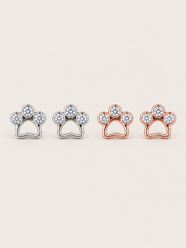 Crystal Paw Print Stud Earrings in Silver and Rose Gold on a warm neutral background