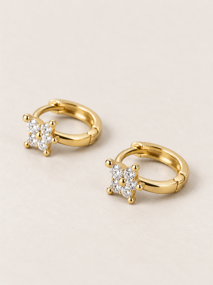 Gold Crystal Star Huggie Earrings shown angled on a warm neutral background