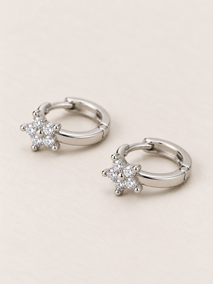 Silver Crystal Star Huggie Earrings shown angled on a warm neutral background