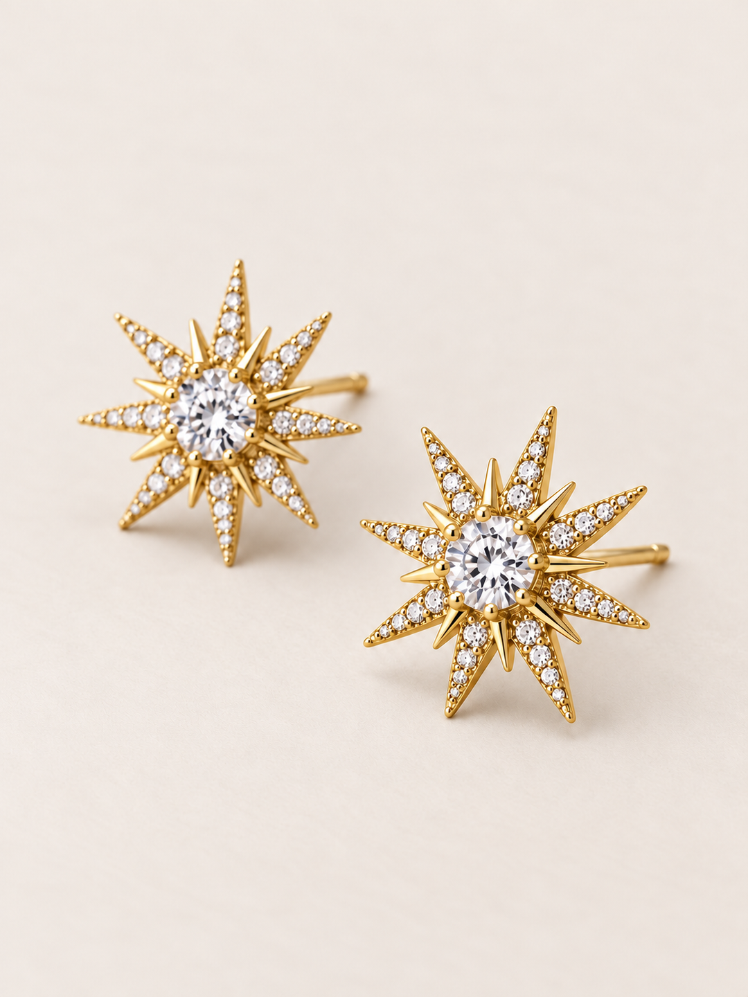 Crystal Starburst Stud Earrings in Gold shown angled on a warm neutral background